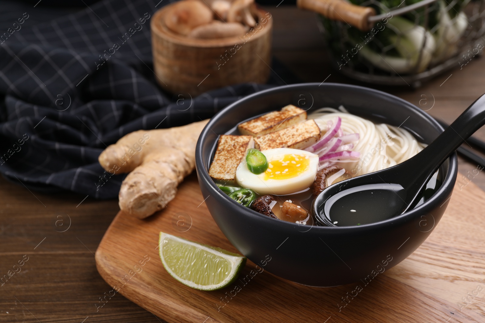 Photo of Delicious vegetarian ramen in bowl and products on wooden table, closeup. Space for text