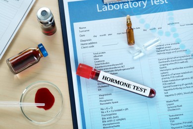 Photo of Hormone test. Sample tube with blood and laboratory form on table, flat lay