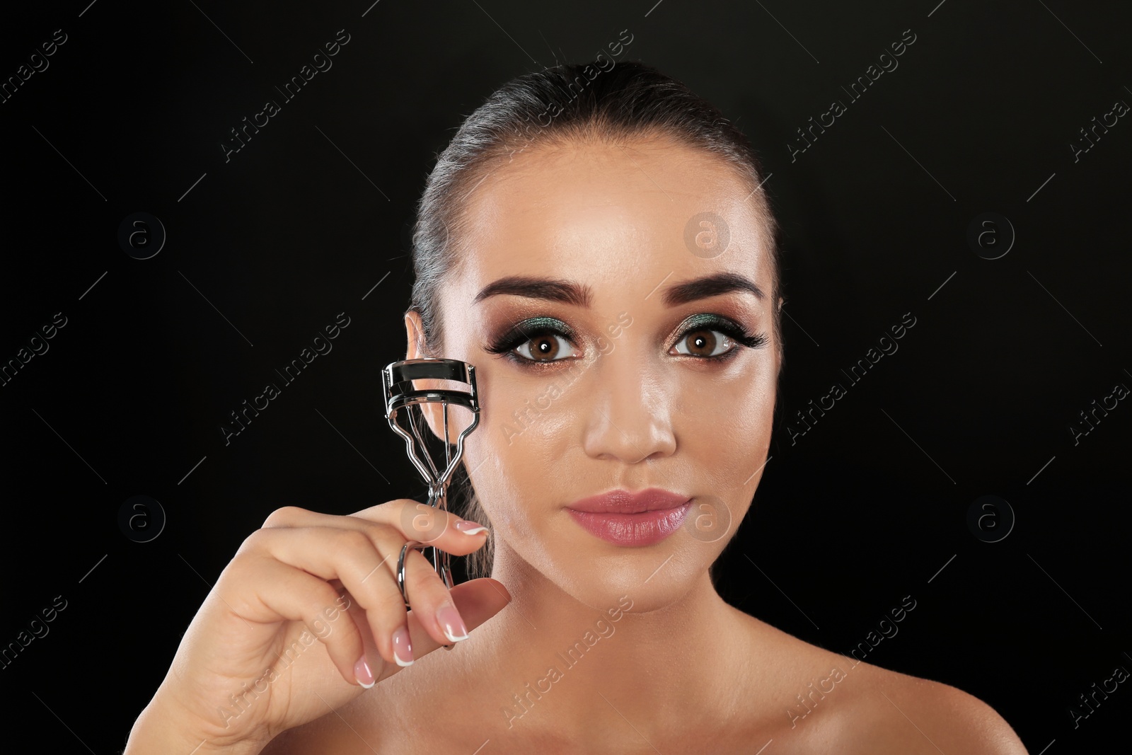 Photo of Portrait of young woman with eyelash extensions holding curler on black background