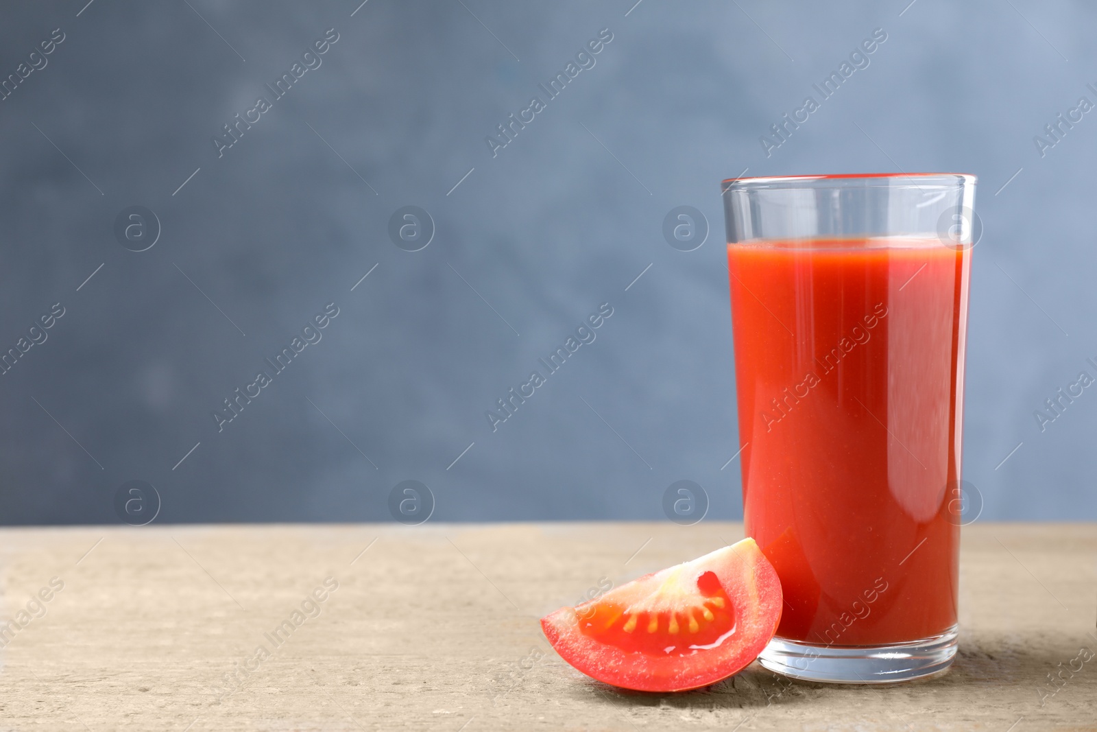 Photo of Delicious fresh juice and slice of tomato on wooden table. Space for text