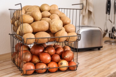 Photo of Container with potatoes and onions on wooden kitchen counter, space for text. Orderly storage