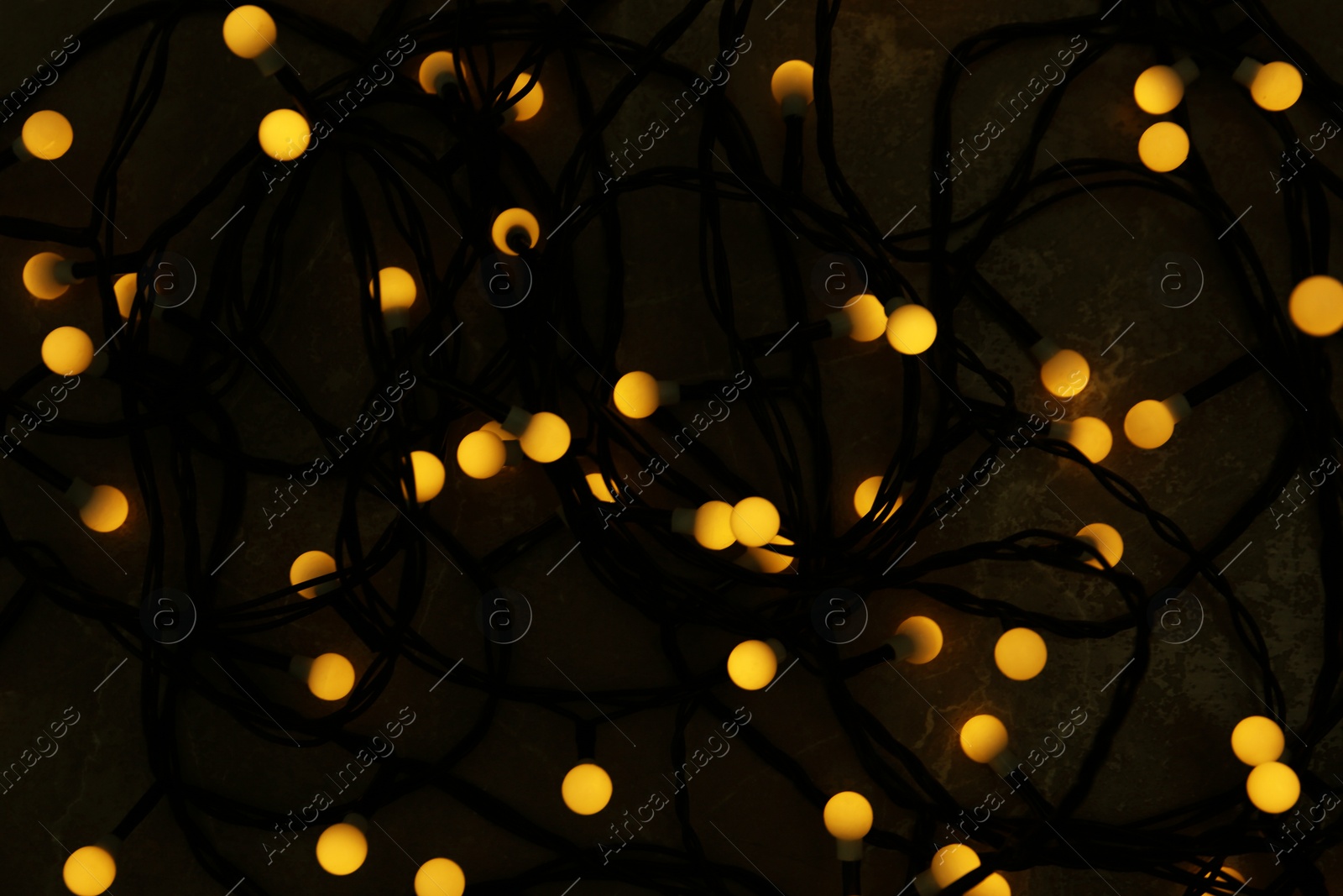 Photo of Glowing Christmas lights on grey marble background, top view