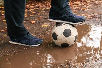 Photo of Man with soccer ball in muddy puddle outdoors, closeup