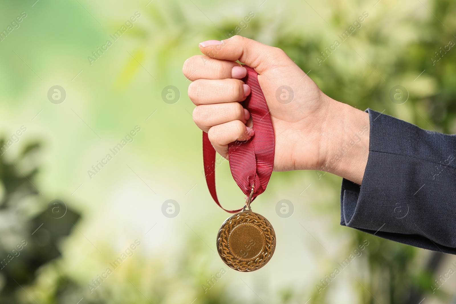 Photo of Woman holding gold medal on blurred background, closeup. Space for text