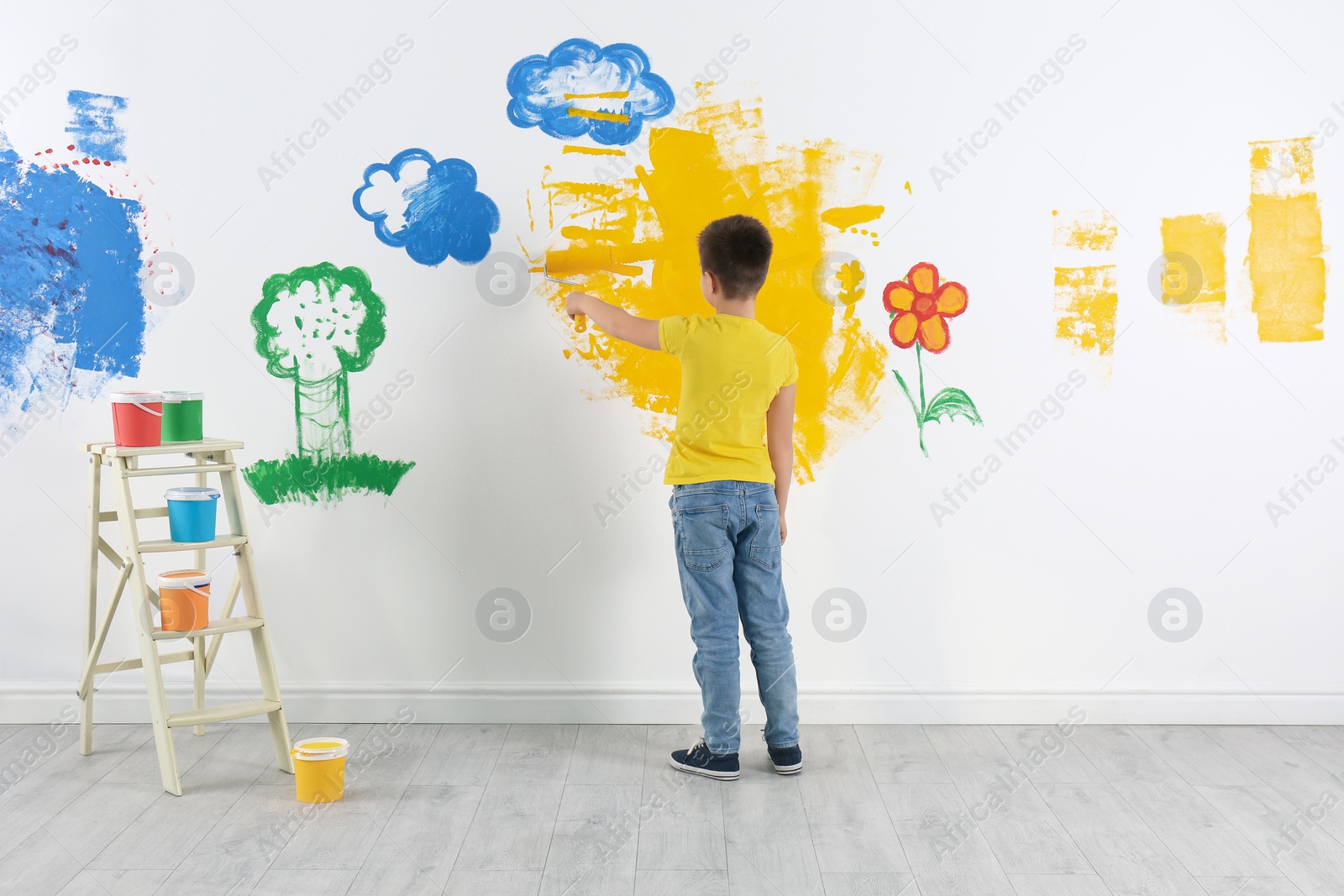 Photo of Little child painting wall with roller brush indoors