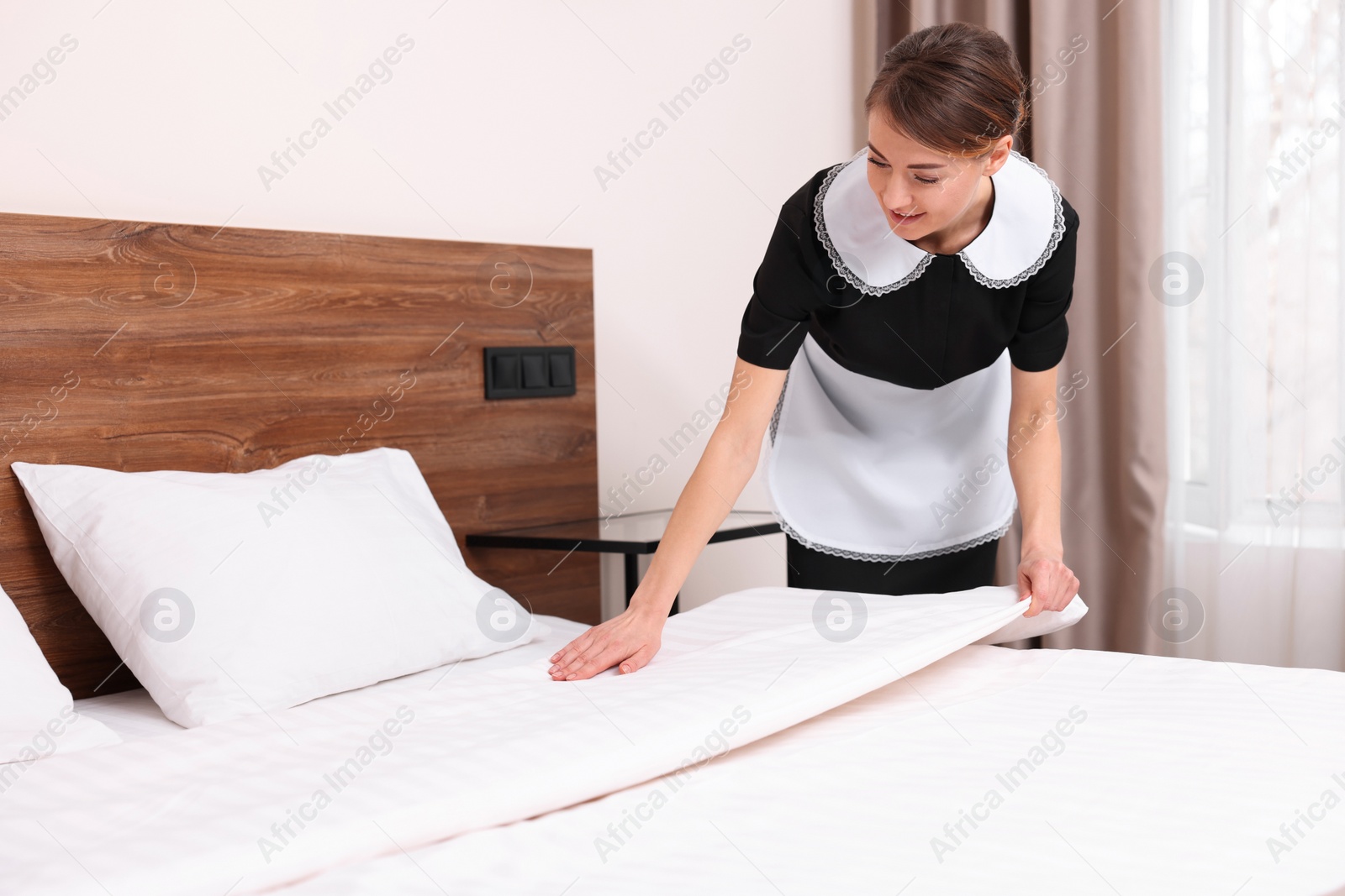 Photo of Beautiful chambermaid making bed in hotel room