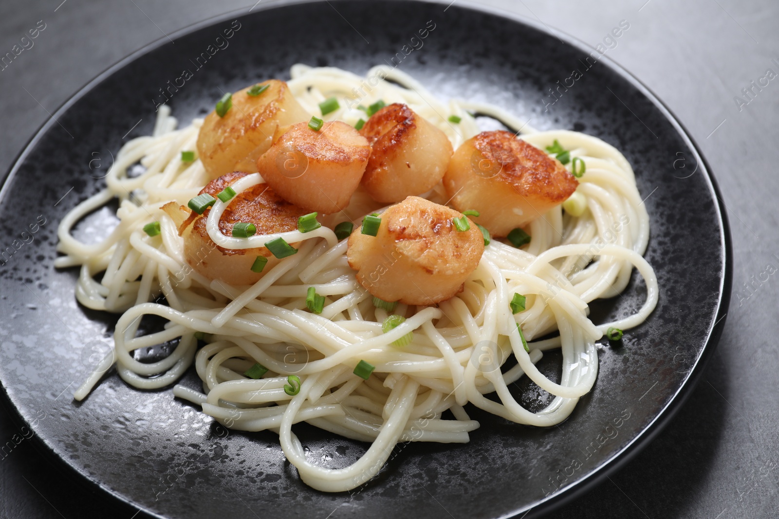 Photo of Delicious scallop pasta with green onion on grey table, closeup