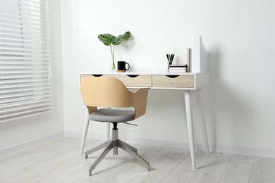 Photo of Comfortable workplace with white desk near wall indoors