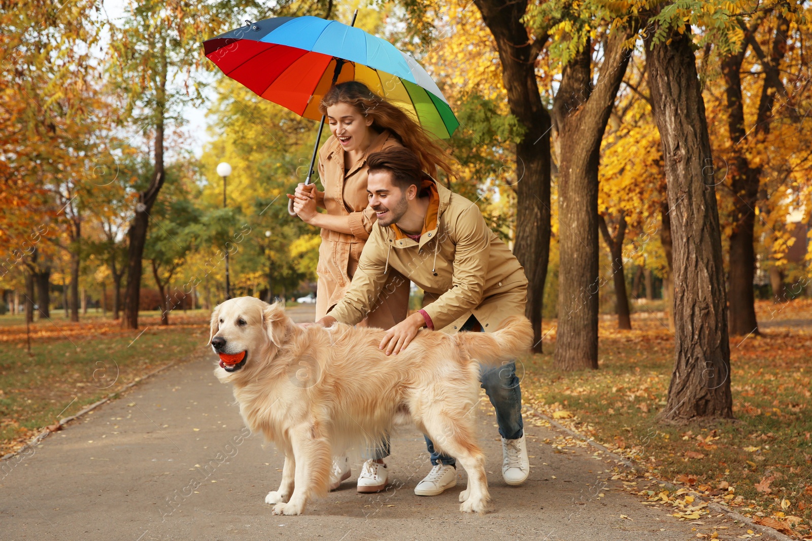 Photo of Young couple with umbrella and dog walking in park