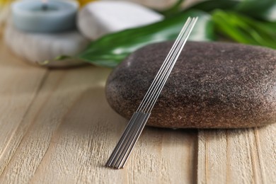 Acupuncture needles and spa stone on wooden table, closeup