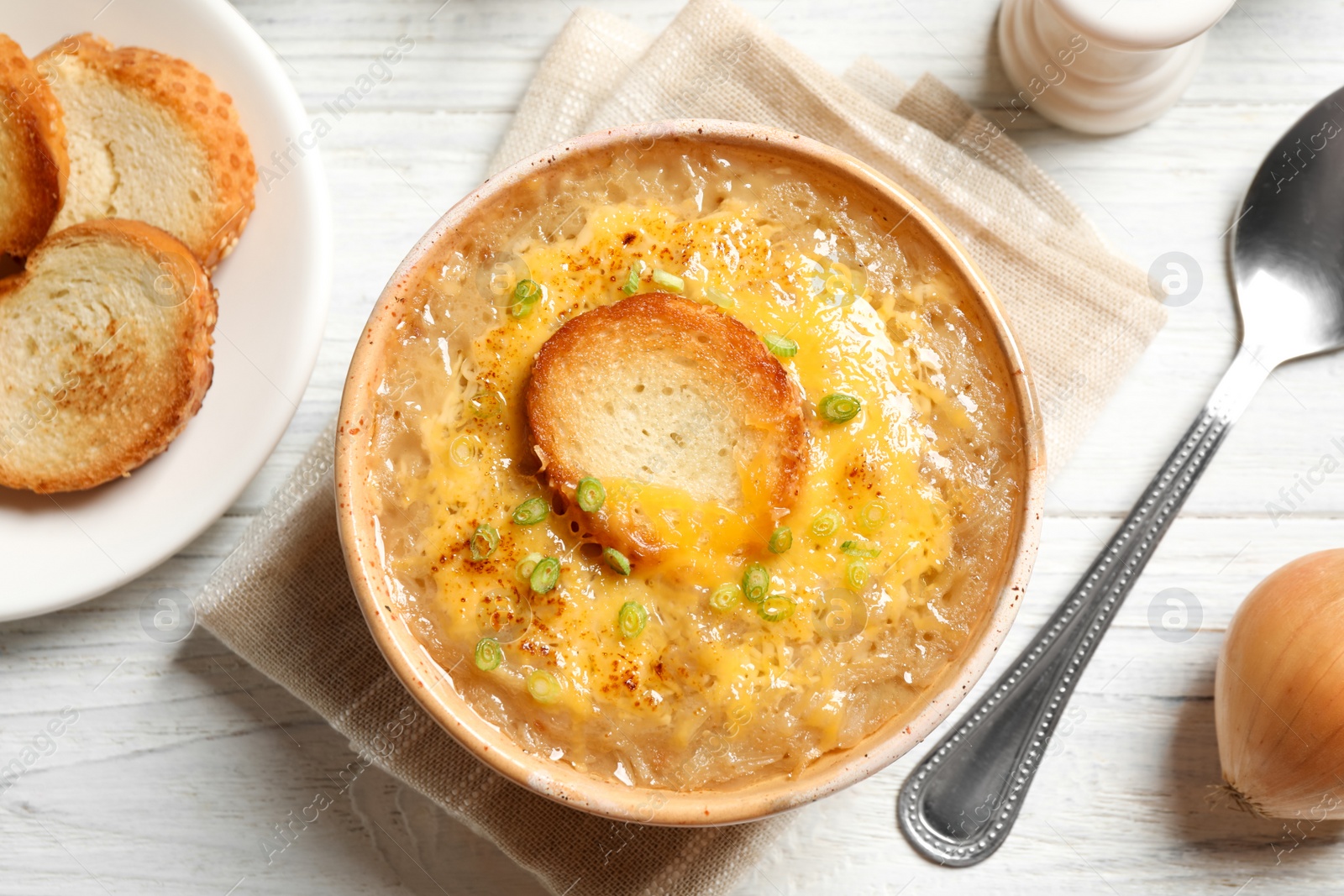 Photo of Tasty homemade french onion soup served on white wooden table, flat lay