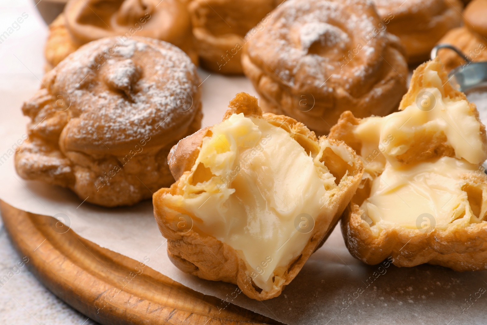 Photo of Delicious profiteroles filled with cream on wooden board, closeup