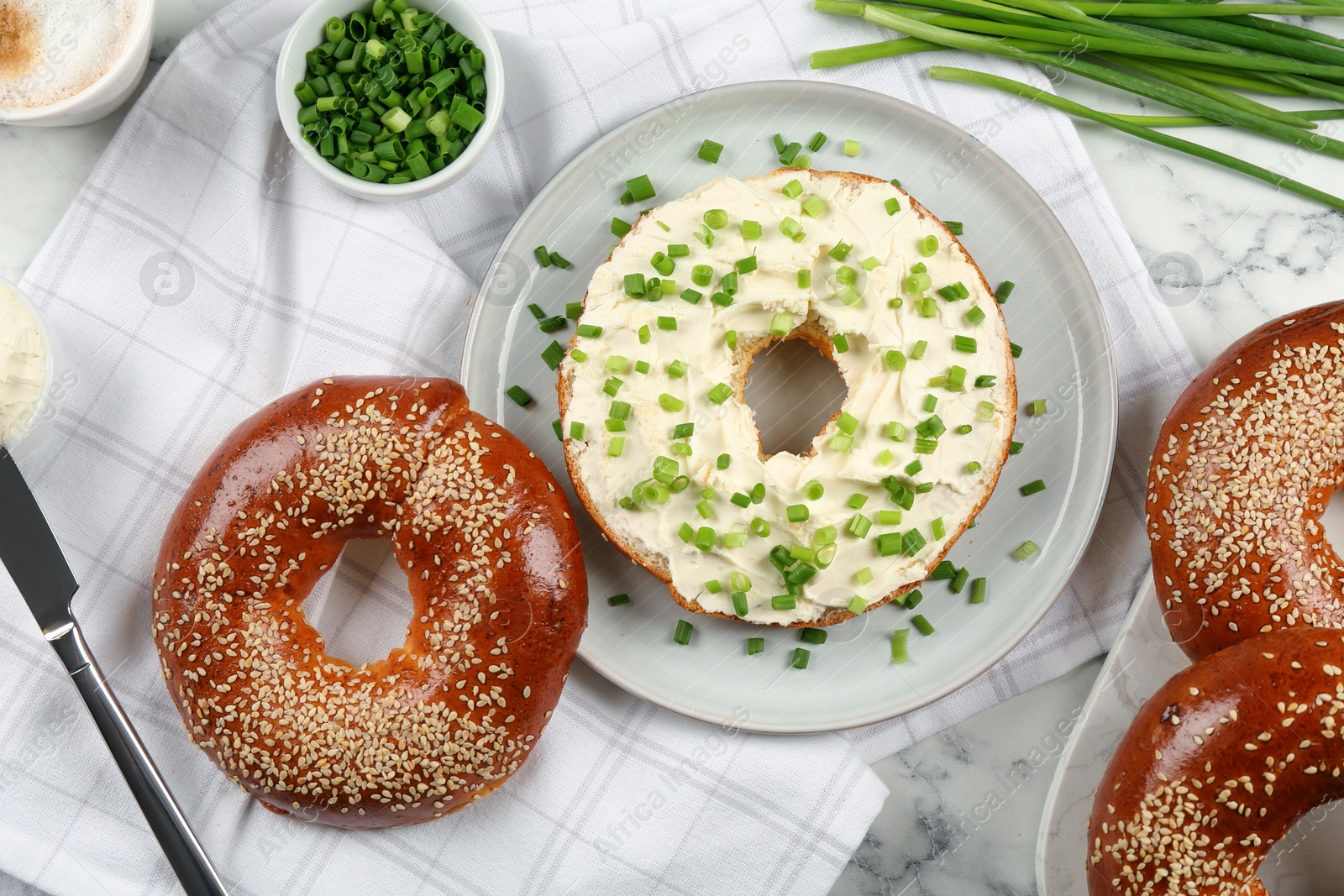 Photo of Delicious bagel with cream cheese and green onion on white marble table, flat lay