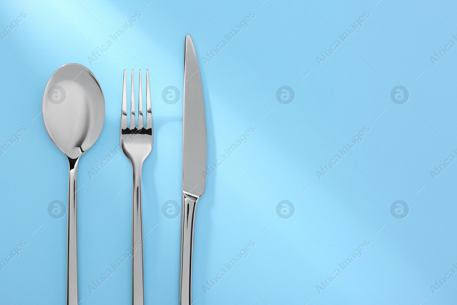 Photo of Spoon, fork and knife on light blue, flat lay. Space for text