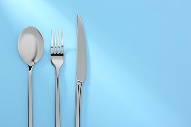 Photo of Spoon, fork and knife on light blue, flat lay. Space for text