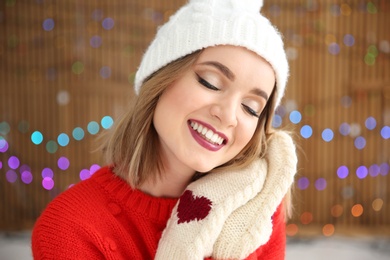Photo of Beautiful young woman in warm clothes posing on blurred lights background. Christmas celebration