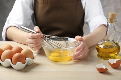 Photo of Woman whisking eggs in glass bowl at wooden table, closeup