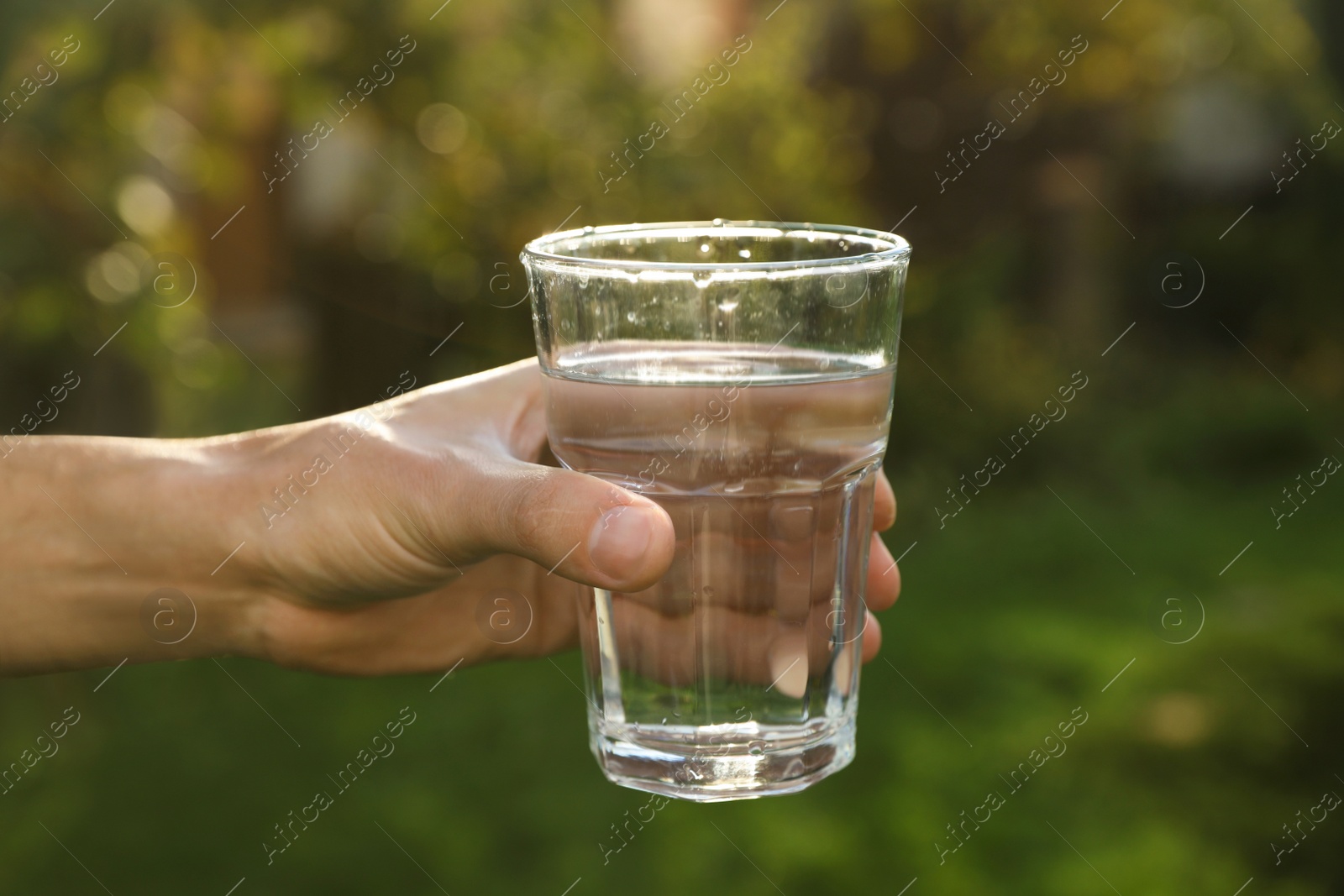 Photo of Man holding glass of fresh water outdoors, closeup