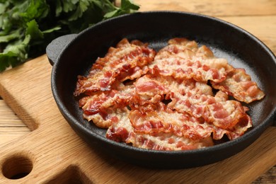 Delicious bacon slices in frying pan on wooden table, closeup