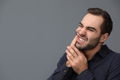 Young man suffering from strong tooth pain on grey background, space for text