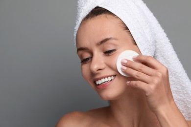Photo of Smiling woman removing makeup with cotton pad on grey background, closeup. Space for text