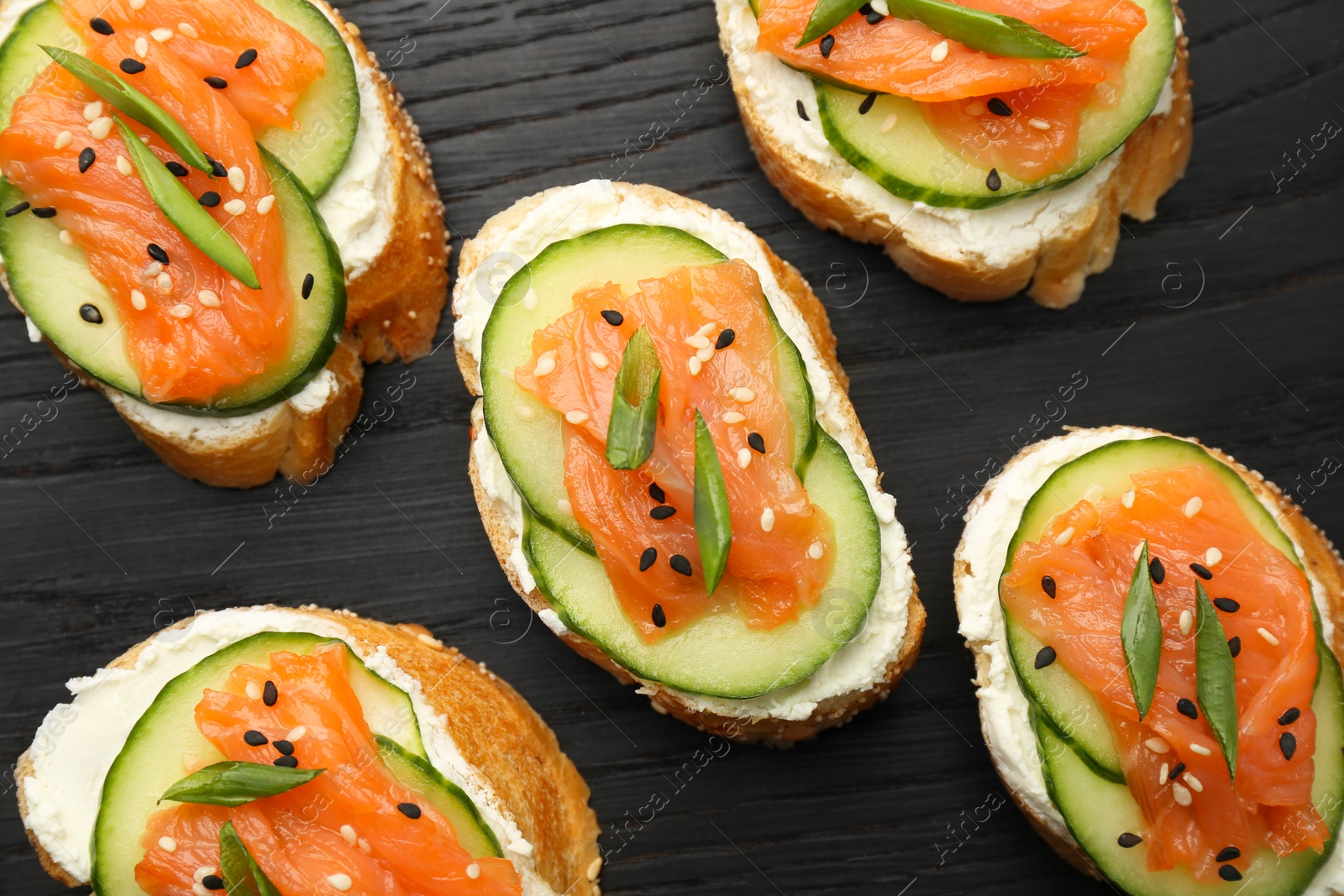 Photo of Tasty canapes with salmon, cucumber and cream cheese on board, top view