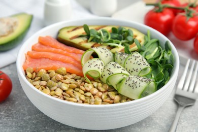 Delicious lentil bowl with salmon, avocado and cucumber on grey table