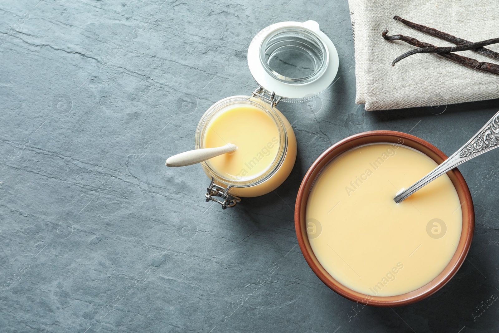 Photo of Flat lay composition with bowl and jar of condensed milk on grey background. Space for text