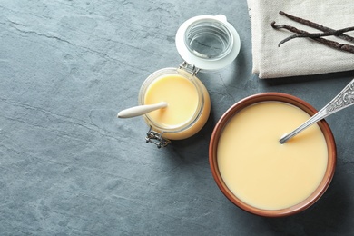 Photo of Flat lay composition with bowl and jar of condensed milk on grey background. Space for text