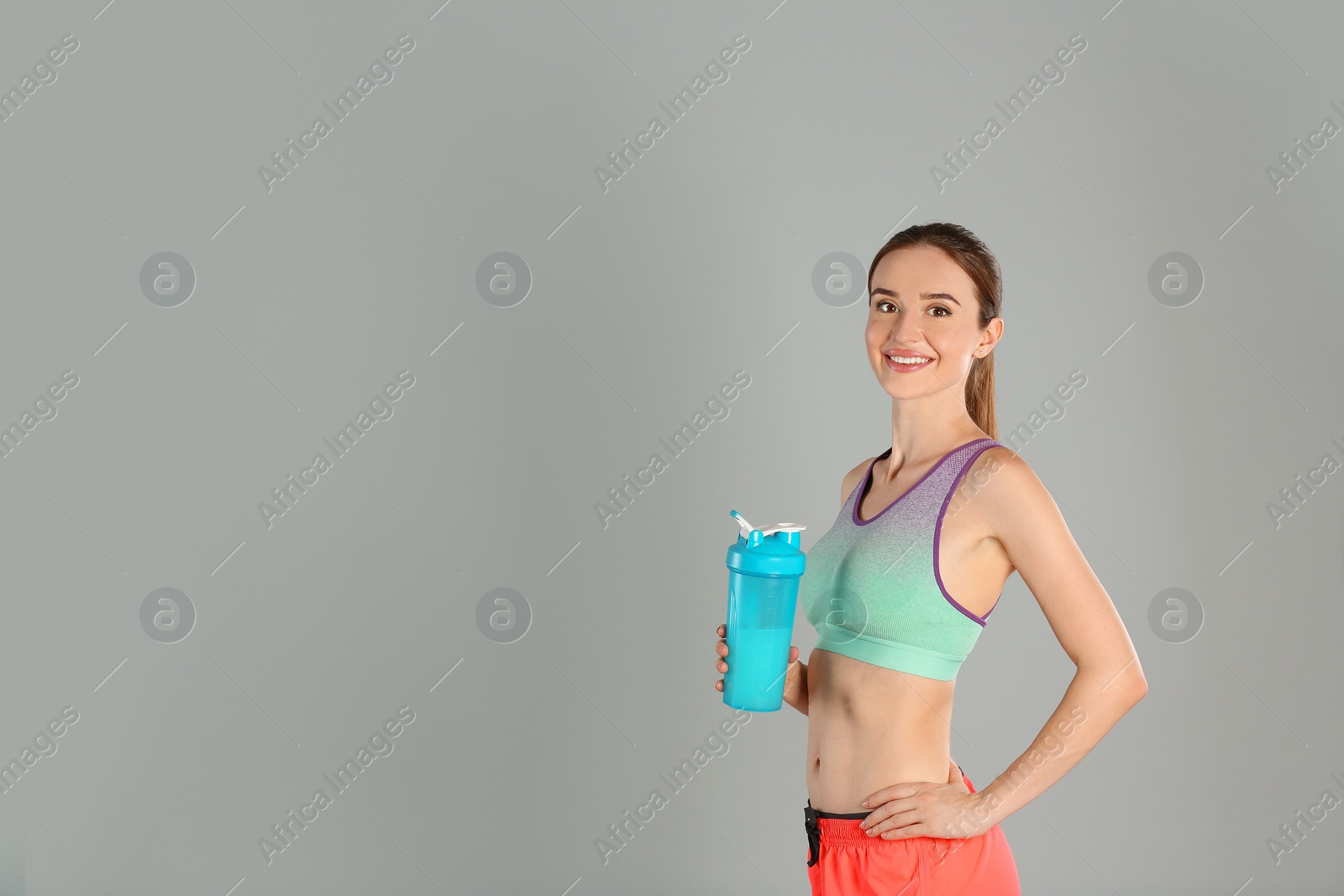 Photo of Athletic young woman with protein shake on light grey background. Space for text