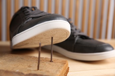Photo of Nails in wooden plank and shoes on table, closeup