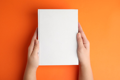 Photo of Woman holding book with blank cover on orange background, top view