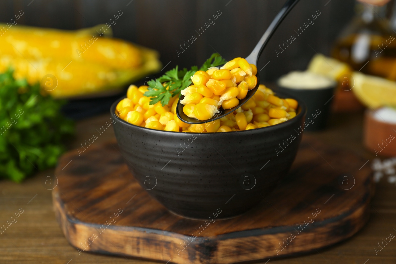 Photo of Bowl and spoon with tasty boiled corn on wooden table