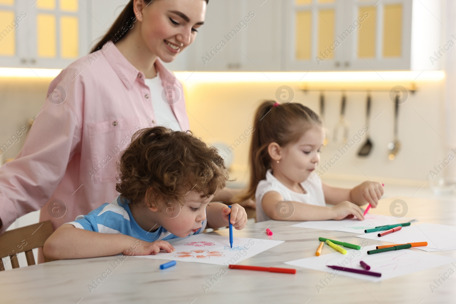 Photo of Mother and her little children drawing with colorful markers at table in kitchen