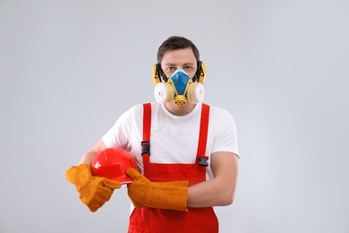 Photo of Male industrial worker in uniform on light background. Safety equipment