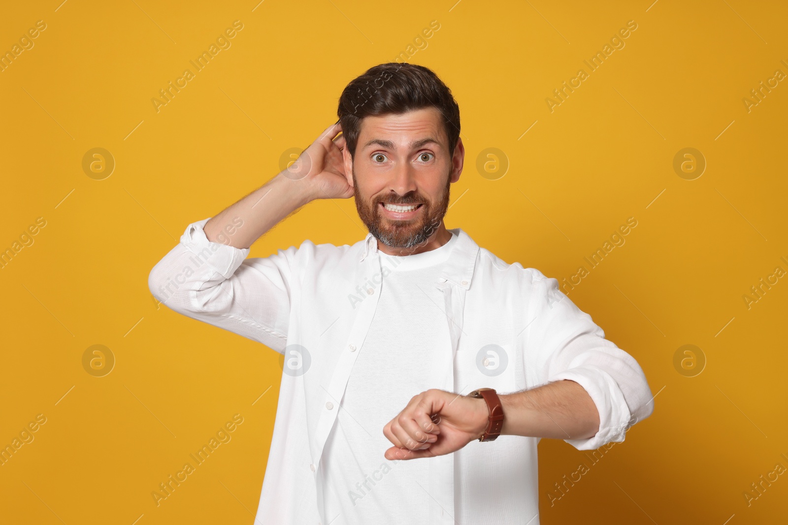 Photo of Emotional man checking time on orange background. Being late concept