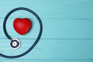 Red heart with stethoscope and space for text on wooden background, flat lay