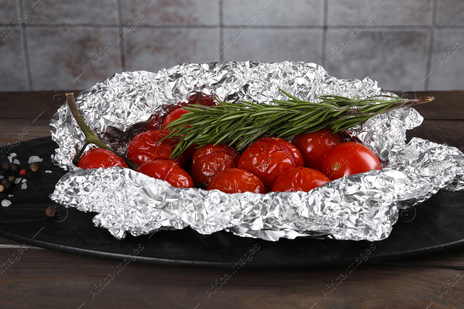 Photo of Aluminum foil with delicious baked tomatoes and rosemary on wooden table