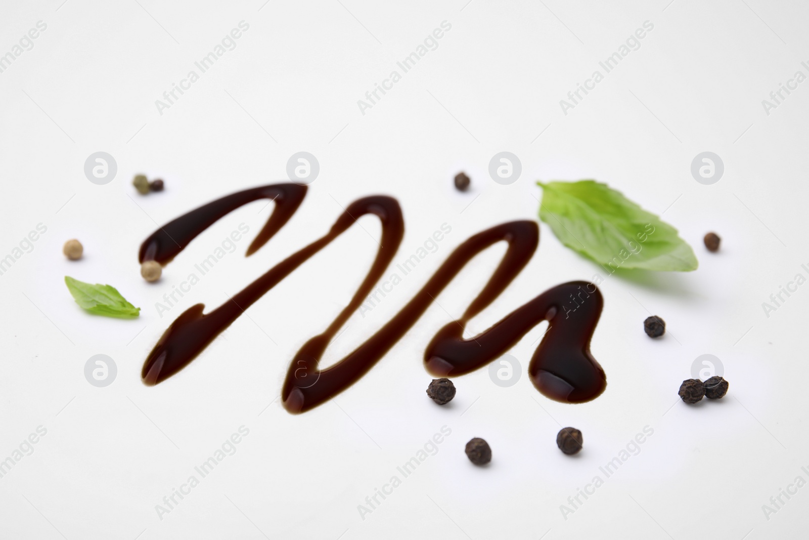 Photo of Organic balsamic vinegar, peppercorns and basil leaves on white background