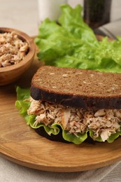 Photo of Delicious sandwich with tuna and lettuce leaves on wooden plate, closeup