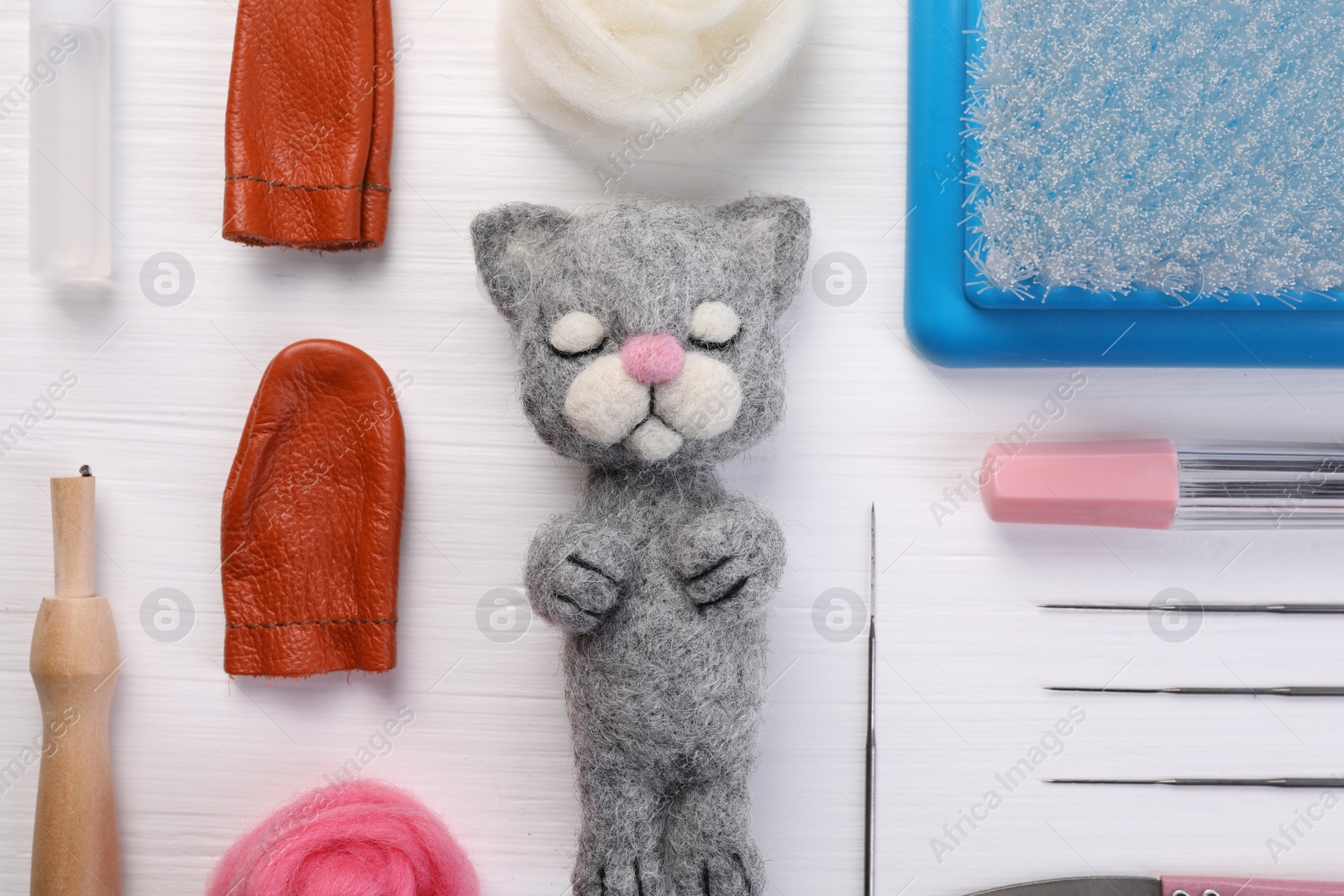 Photo of Felted cat, wool and different tools on white wooden table, flat lay
