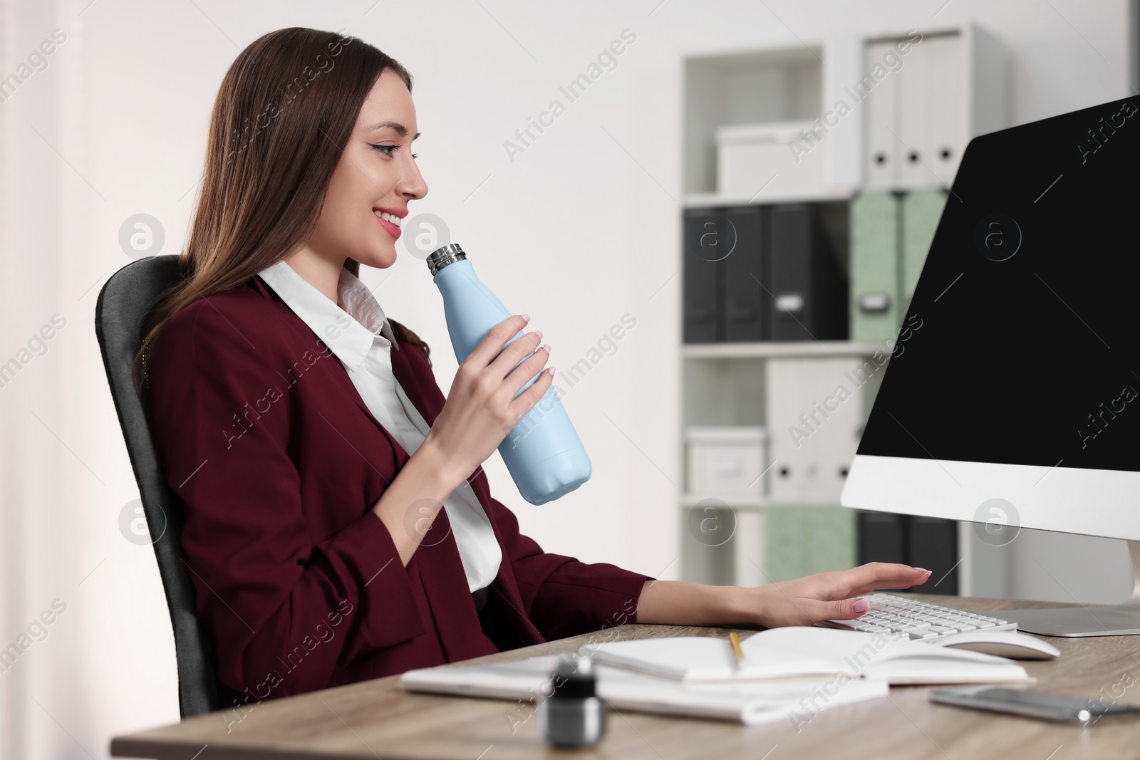 Photo of Woman holding light blue thermos bottle at workplace