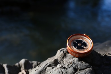 Photo of Compass on rock near river outdoors. Space for text