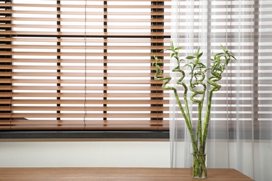 Photo of Vase with bamboo stems on wooden table indoors, space for text