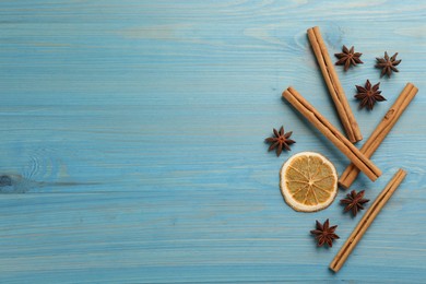 Photo of Aromatic cinnamon sticks, dry orange and anise on light blue wooden table, flat lay. Space for text