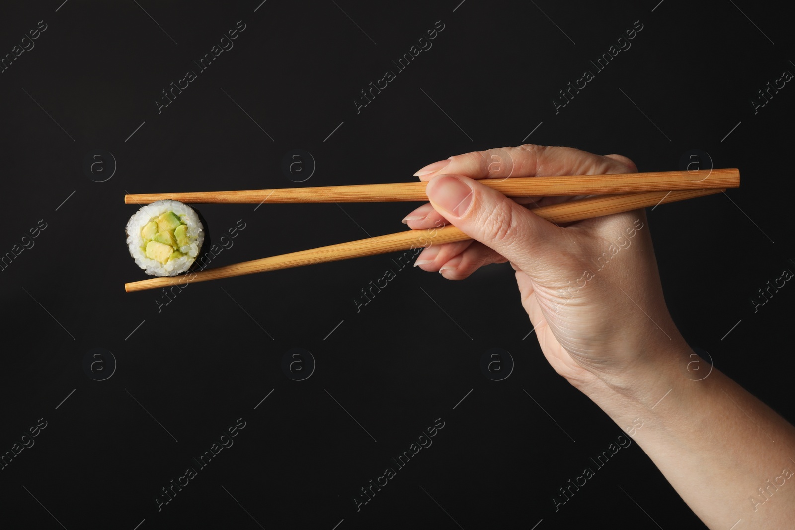 Photo of Woman holding sushi roll with chopsticks on black background, closeup