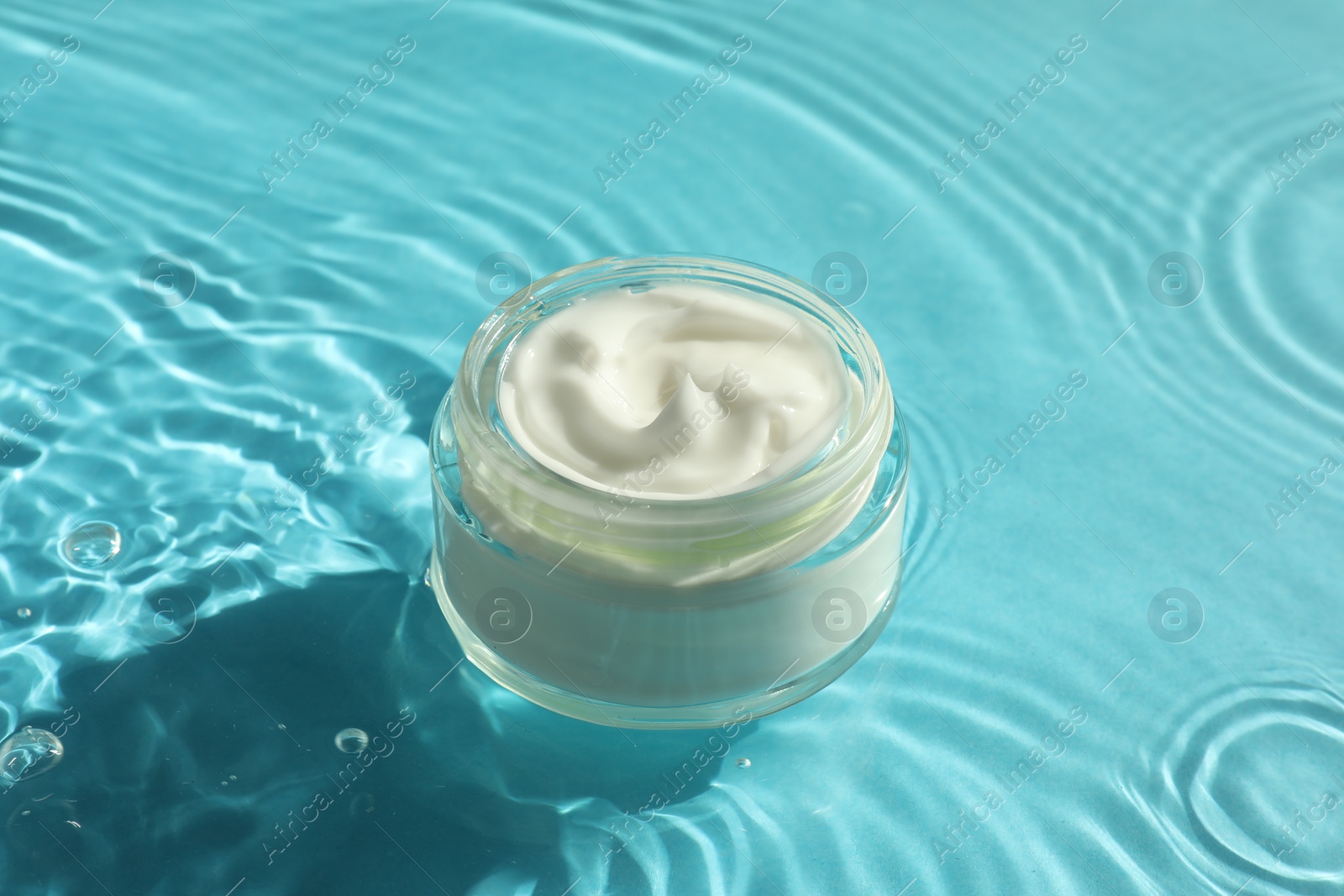 Photo of Jar with moisturizing cream in water on light blue background