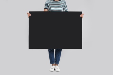 Woman holding blank poster on light grey background, closeup