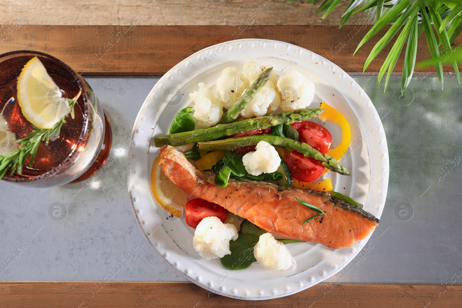 Photo of Healthy meal. Piece of tasty grilled salmon with vegetables and glass of refreshing drink on wooden table, top view