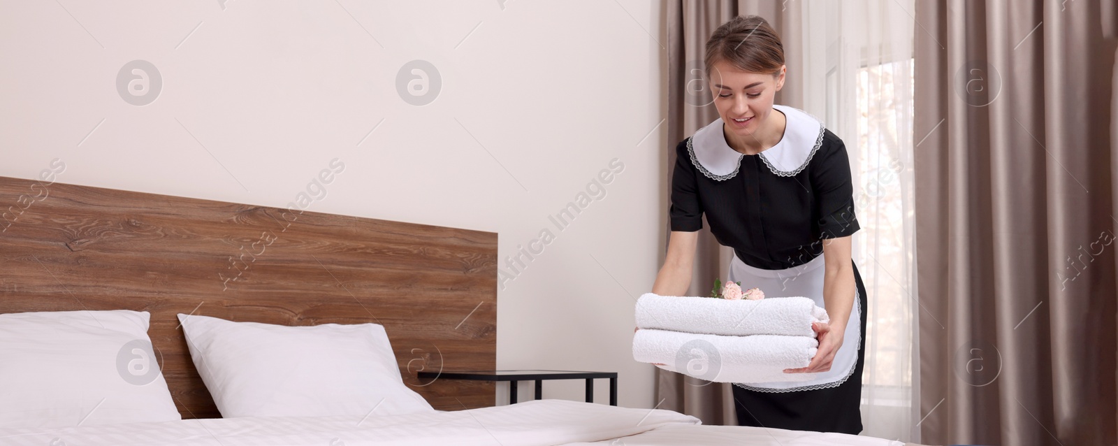 Image of Beautiful chambermaid putting fresh towels on bed in hotel room. Banner design